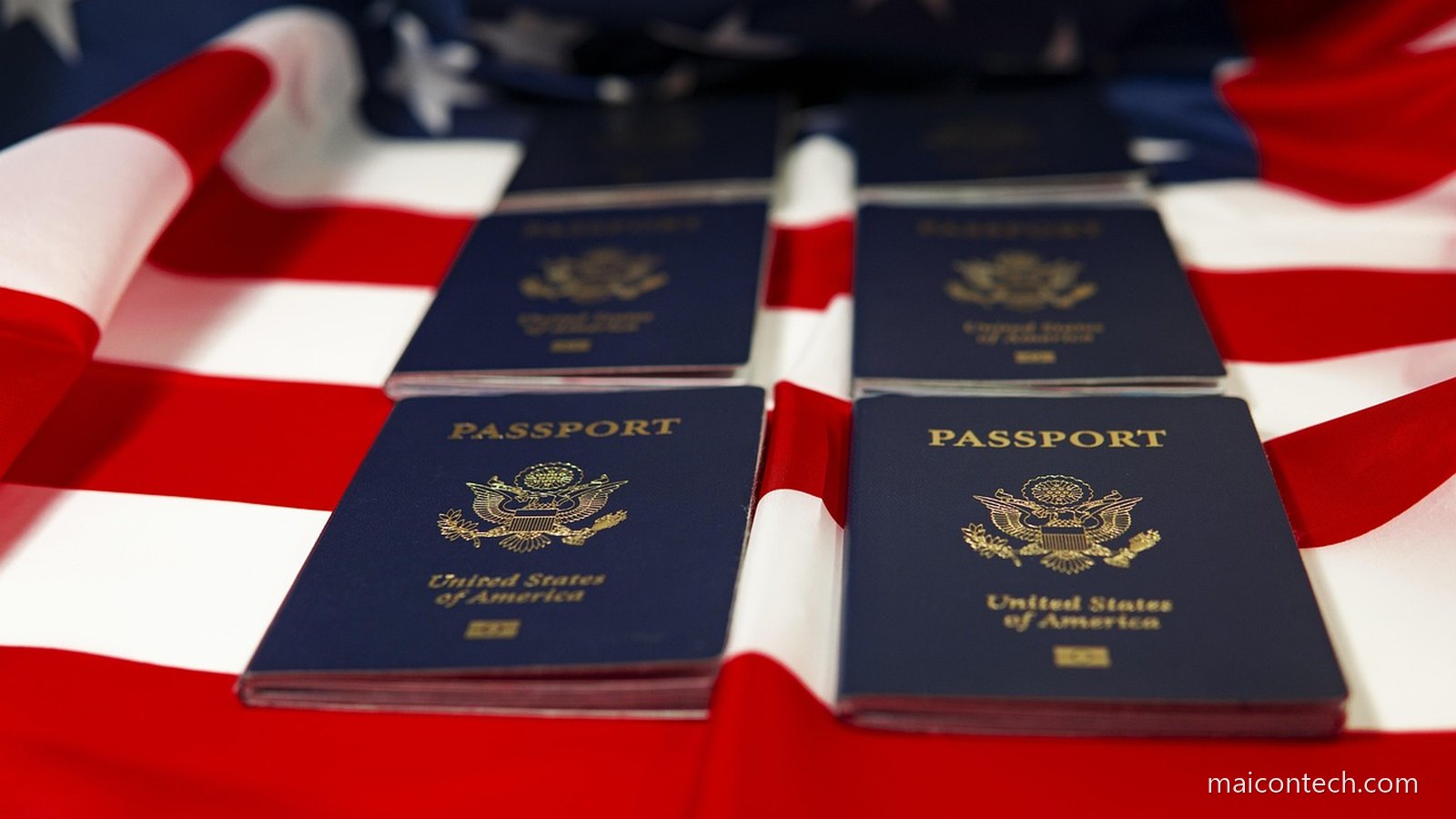 Quatro passaportes azuis dos Estados Unidos pousados sobre a bandeira americana, com o brasao dourado visivel nas capas